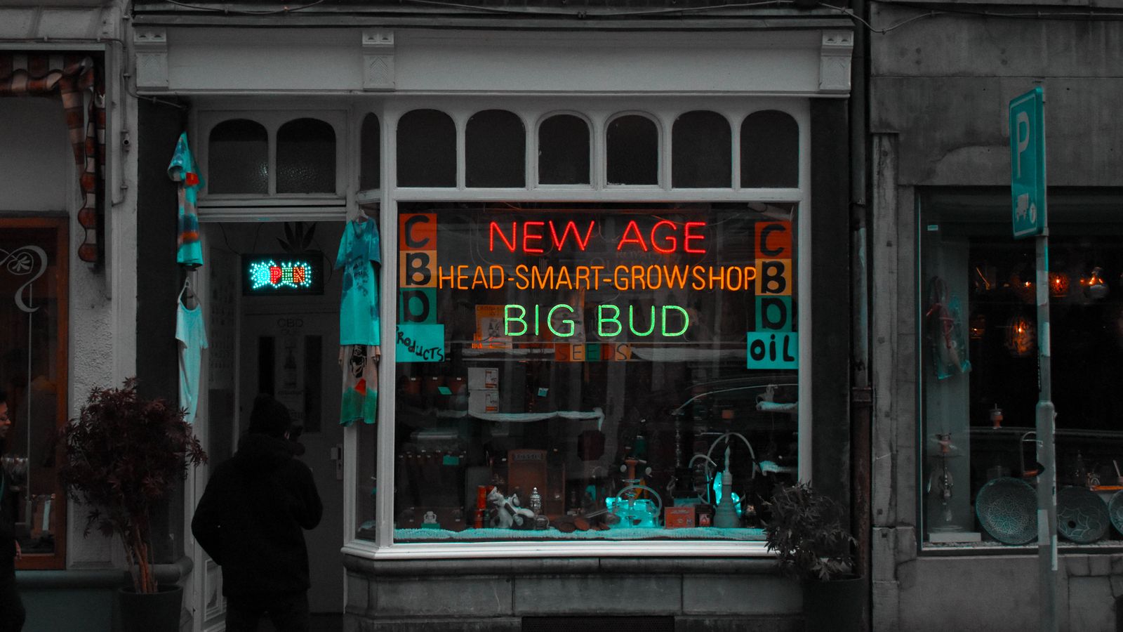 Street view of an urban CBD shop with neon signs and passerby at night.