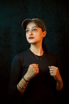 A confident woman posing in a boxing stance with a dark background.