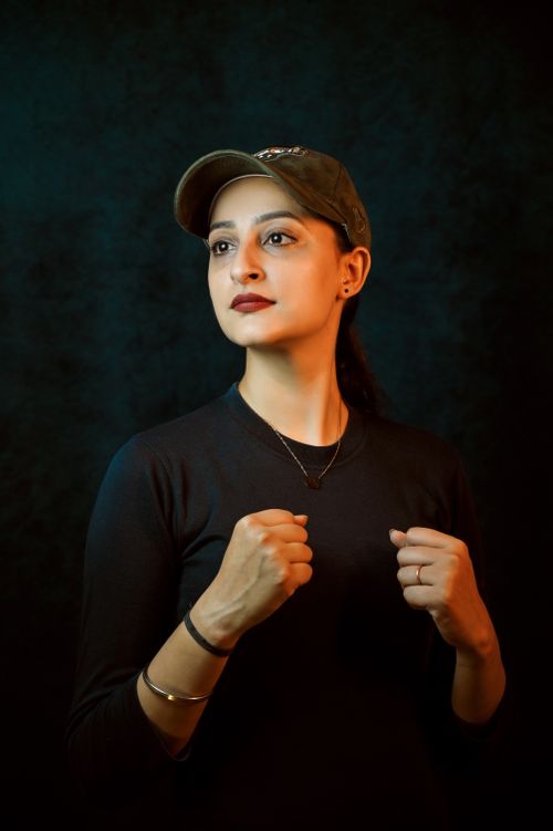 Free A confident woman posing in a boxing stance with a dark background. Stock Photo