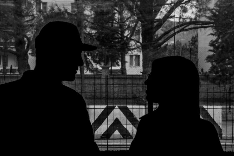 Silhouette Of Couple Standing Near Fence In Black And White