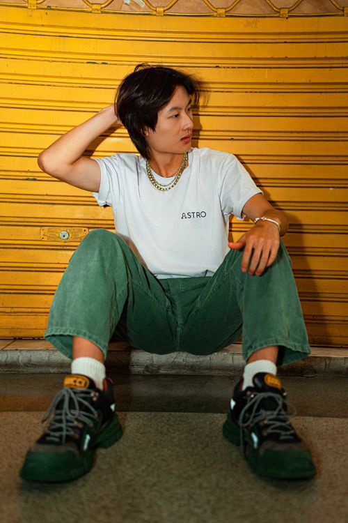 Free Stylish young man in casual outfit sitting against a vibrant yellow wall. Stock Photo