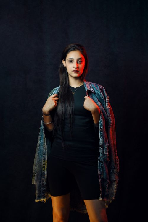 Free Stylish portrait of a young adult woman with a denim jacket and dark backdrop. Stock Photo