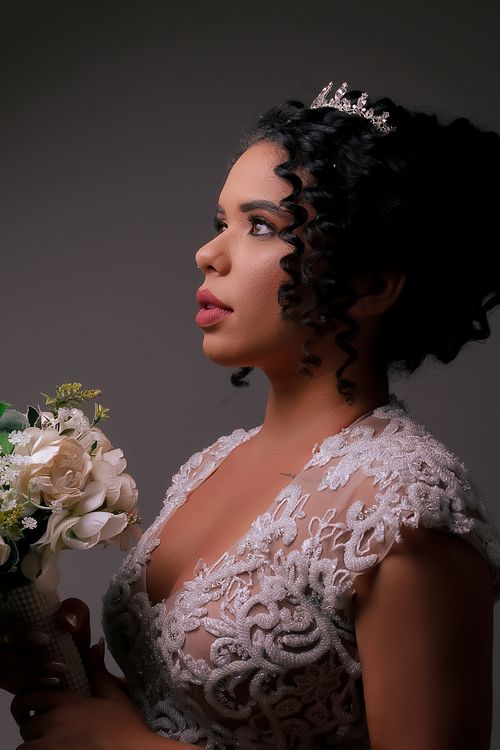 Free A bride with curly hair poses elegantly with a floral bouquet against a gray background. Stock Photo