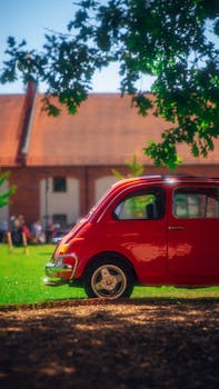 A classic red car shines in a rural landscape during summer, evoking travel nostalgia.