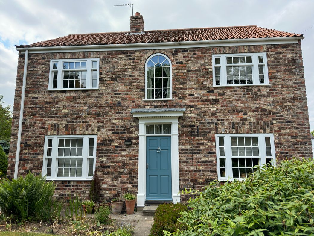 Illustrative red-brick English home with white-framed windows and a blue front door