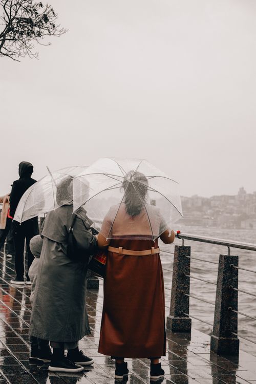 Free Group of people with umbrellas enjoying a rainy day walk by the seashore promenade. Stock Photo