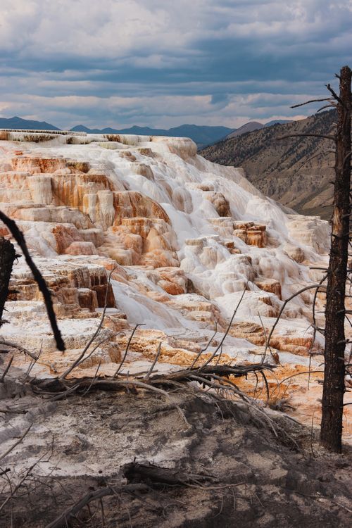 Free Majestic view of geothermal terraces in Yellowstone with cloudy skies and rugged terrain. Stock Photo
