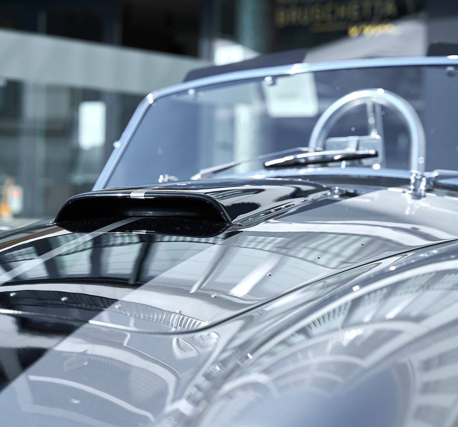 Close-up of a modern car hood reflecting light in a sunlit indoor setting.