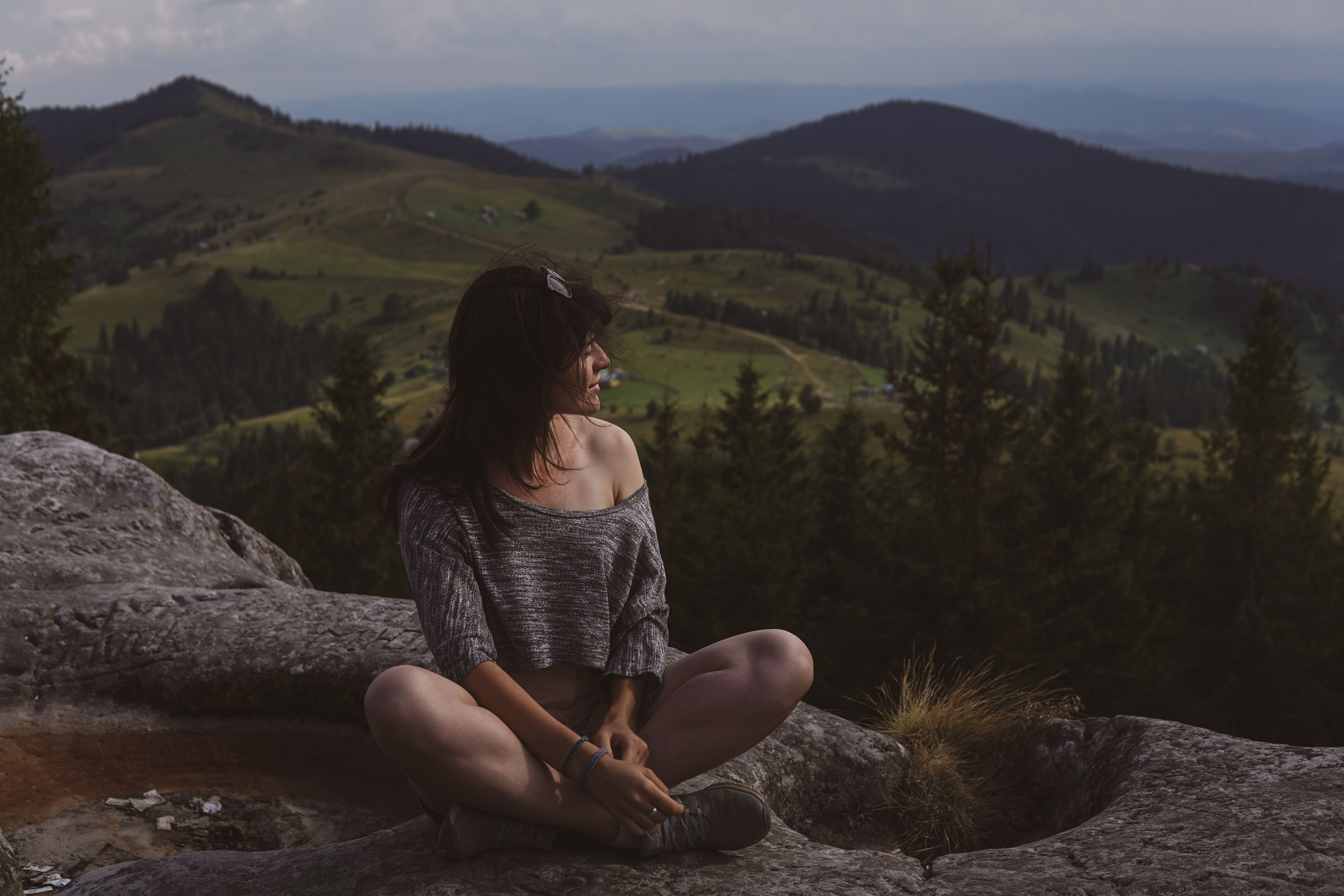 A woman sits on a mountain rock enjoying a scenic view of a lush green valley at daytime.