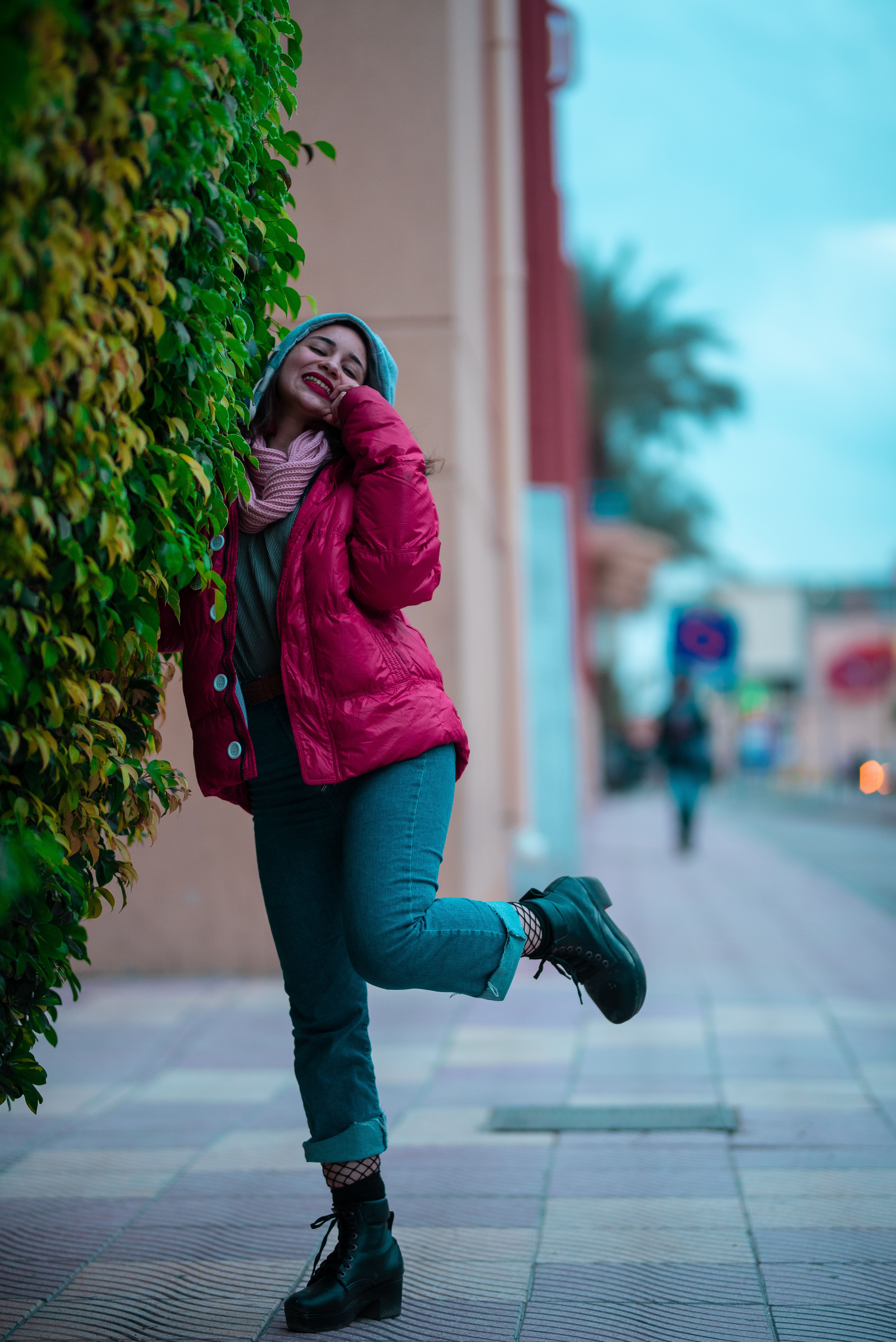 Woman in a pink jacket posing playfully on a city street, exuding joy.