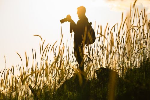 Free A photographer silhouetted against a sunset, standing in a grassy field in Türkiye. Stock Photo