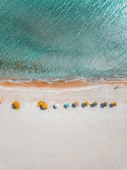 Aerial view of vibrant beach umbrellas on the shore with turquoise waves gently crashing.