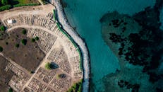 航拍镜头沿着岩石海岸线，捕捉到古代废墟与碧绿海水，展现出风景优美的沿海美景