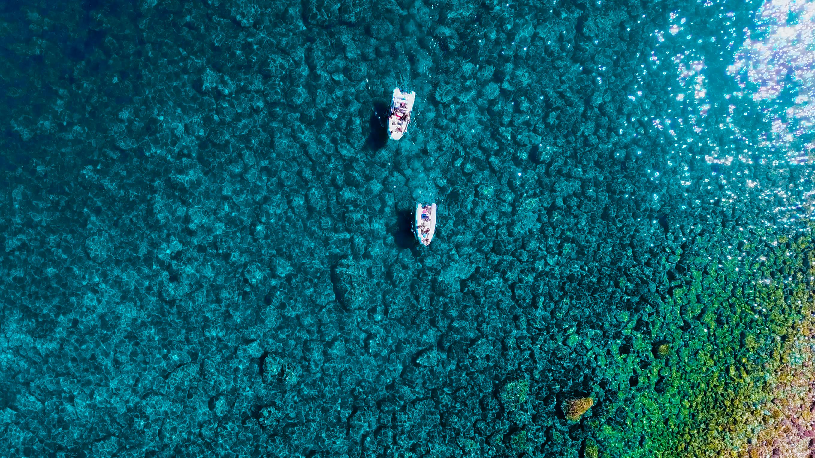 从空中俯瞰，两艘船行驶在碧绿的大海上，珊瑚礁清晰可见，景象令人惊叹