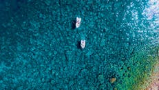 从空中俯瞰，两艘船行驶在碧绿的大海上，珊瑚礁清晰可见，景象令人惊叹