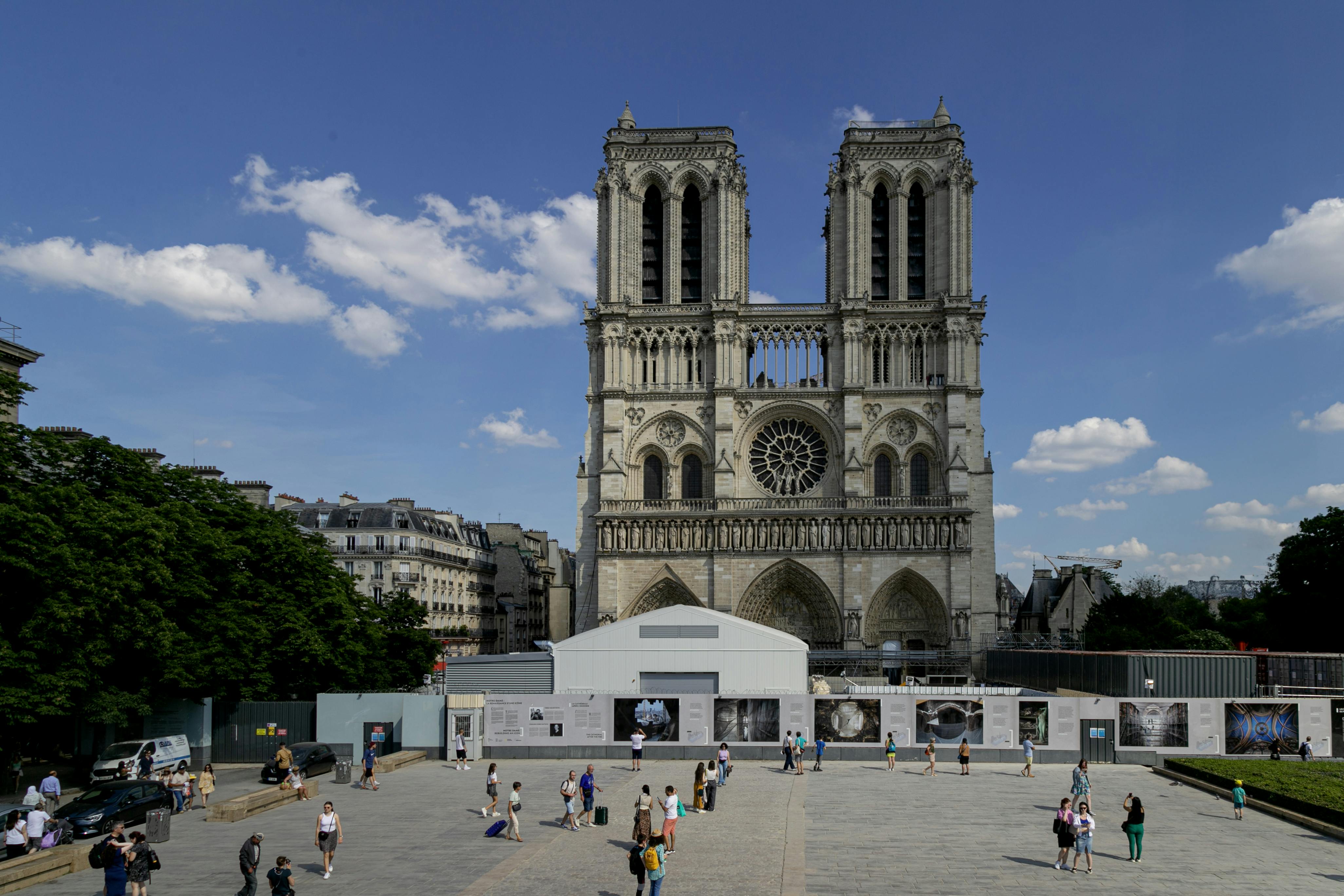 Front view of Notre-Dame Cathedral, Paris on a sunny day with tourists in the square.