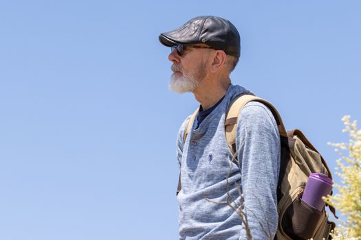 Portrait of an elderly man with a backpack hiking outdoors under a clear blue sky.