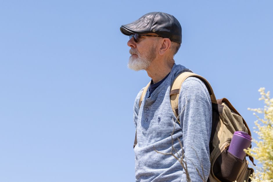 Portrait of an elderly man with a backpack hiking outdoors under a clear blue sky.