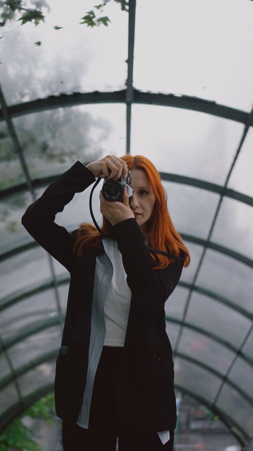 Free Redheaded woman taking a photo under an arched glass ceiling. Stock Photo