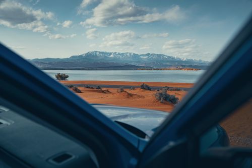 Free Capture a stunning view of desert sands, lake, and distant snowcapped mountains from inside a car. Stock Photo