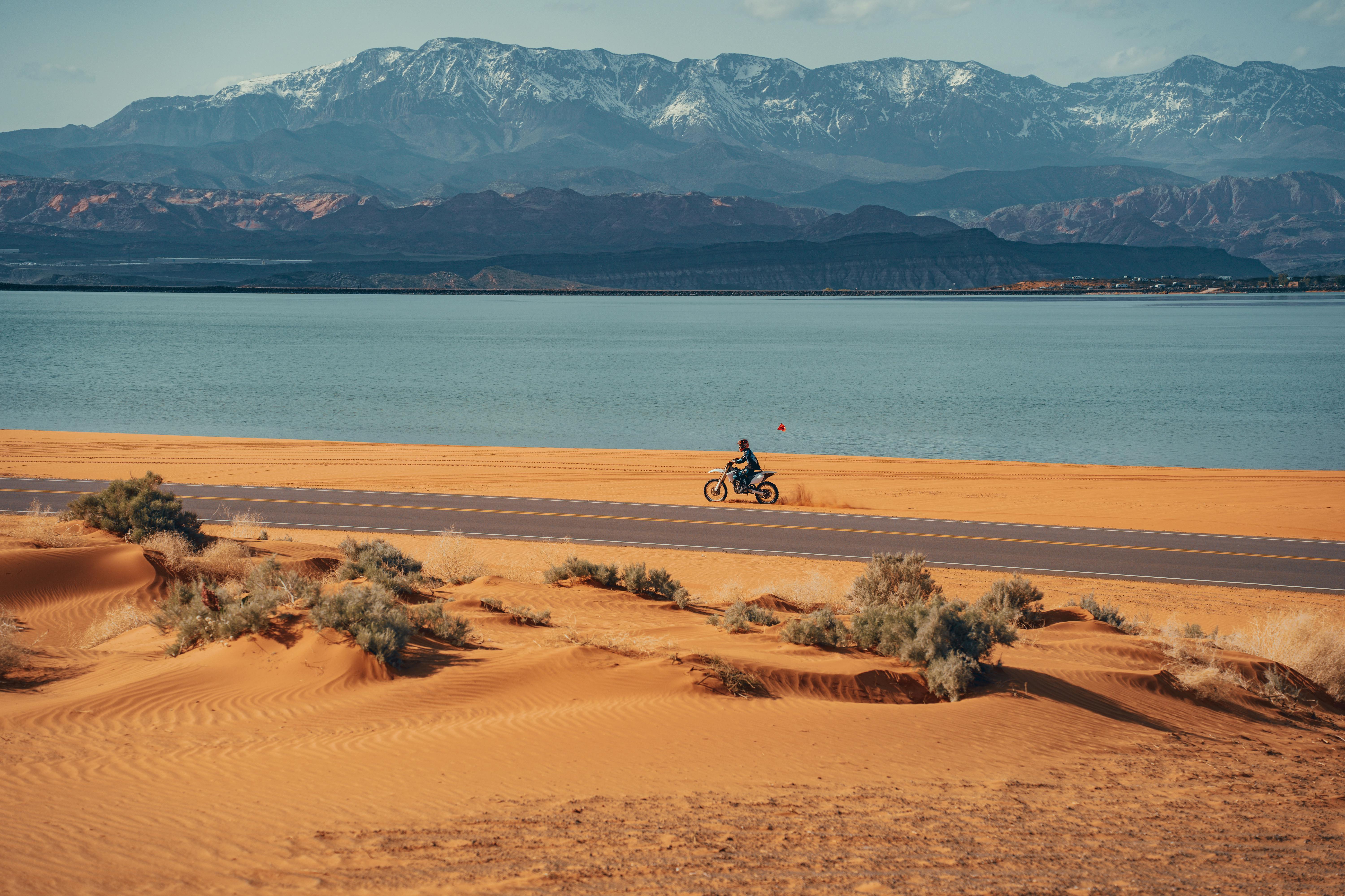 Motorbike rider exploring a scenic desert landscape with mountains and a lake in the background.