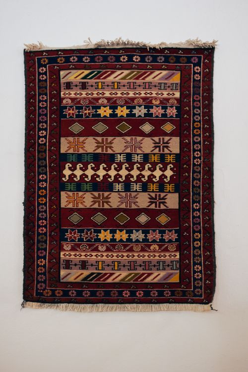 Free Intricate Diyarbakır kilim rug with colorful geometric patterns, displayed on a white wall. Stock Photo