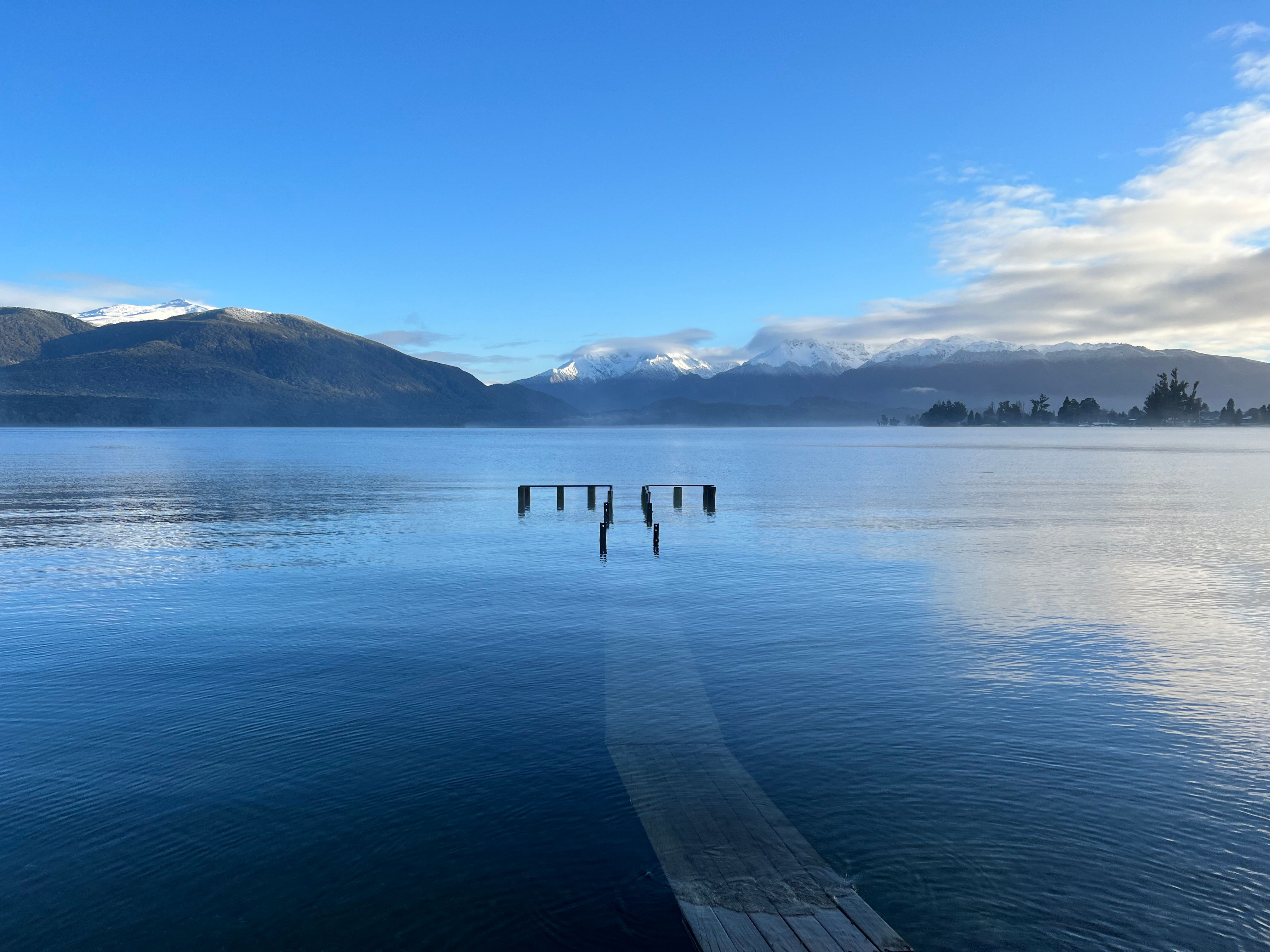 Peaceful lake with a distant view of snow-covered mountains in Southland, New Zealand.