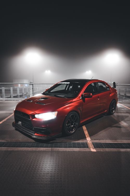Free Stylish red Mitsubishi Lancer Evolution illuminated at night in an empty parking lot, showcasing its sleek design. Stock Photo