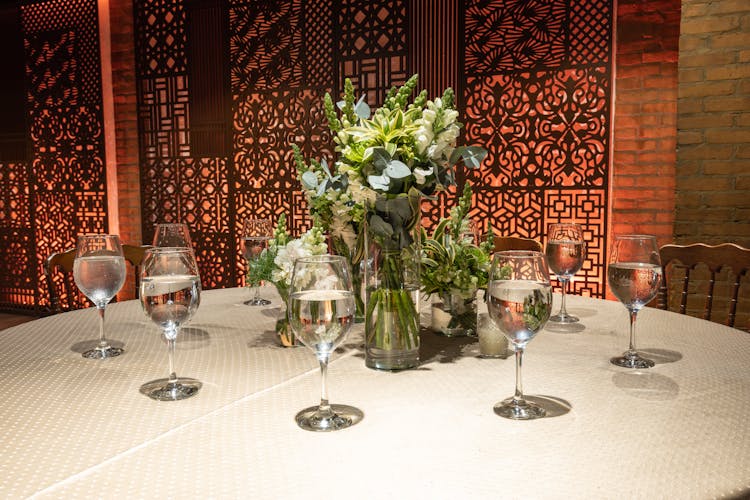 Bouquet Of Flowers In Vase Surrounded By Wine Glasses Filled With Water