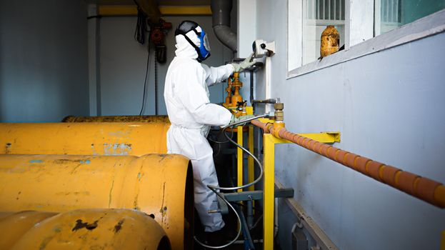 A man in white protective gear is working on a large yellow barrel