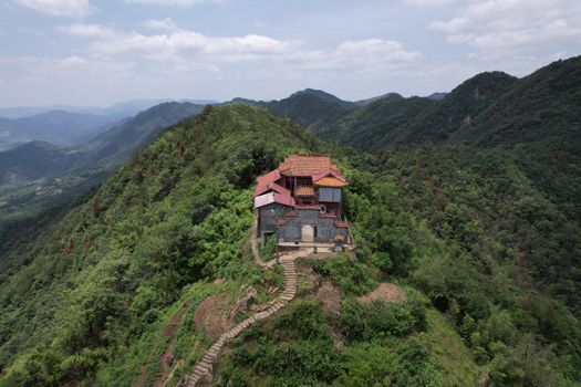 Aerial view of a traditional temple situated on a lush green mountain under a bright blue sky.