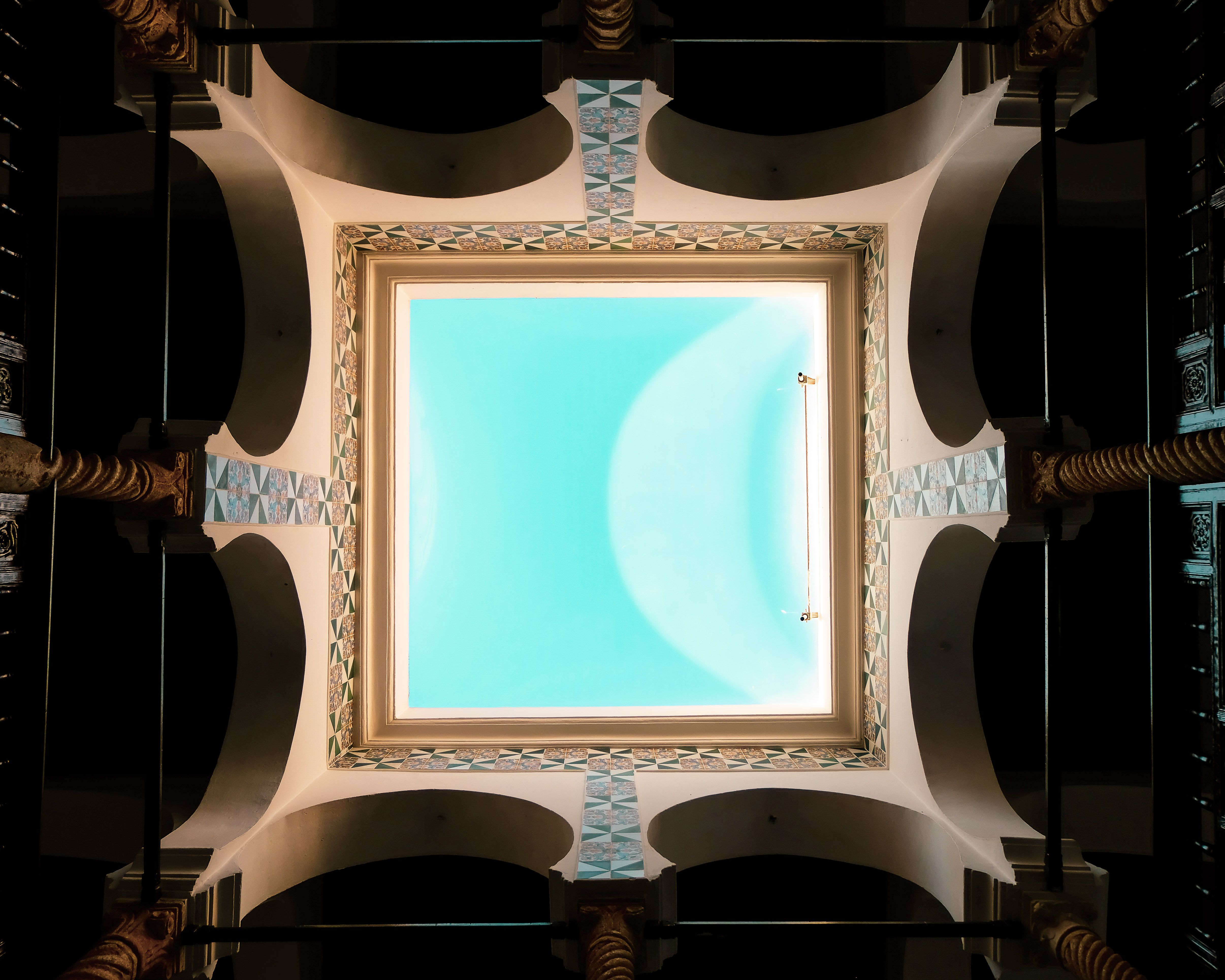 View of a skylight framed by ornate arches and geometric patterns. Bright blue sky visible.