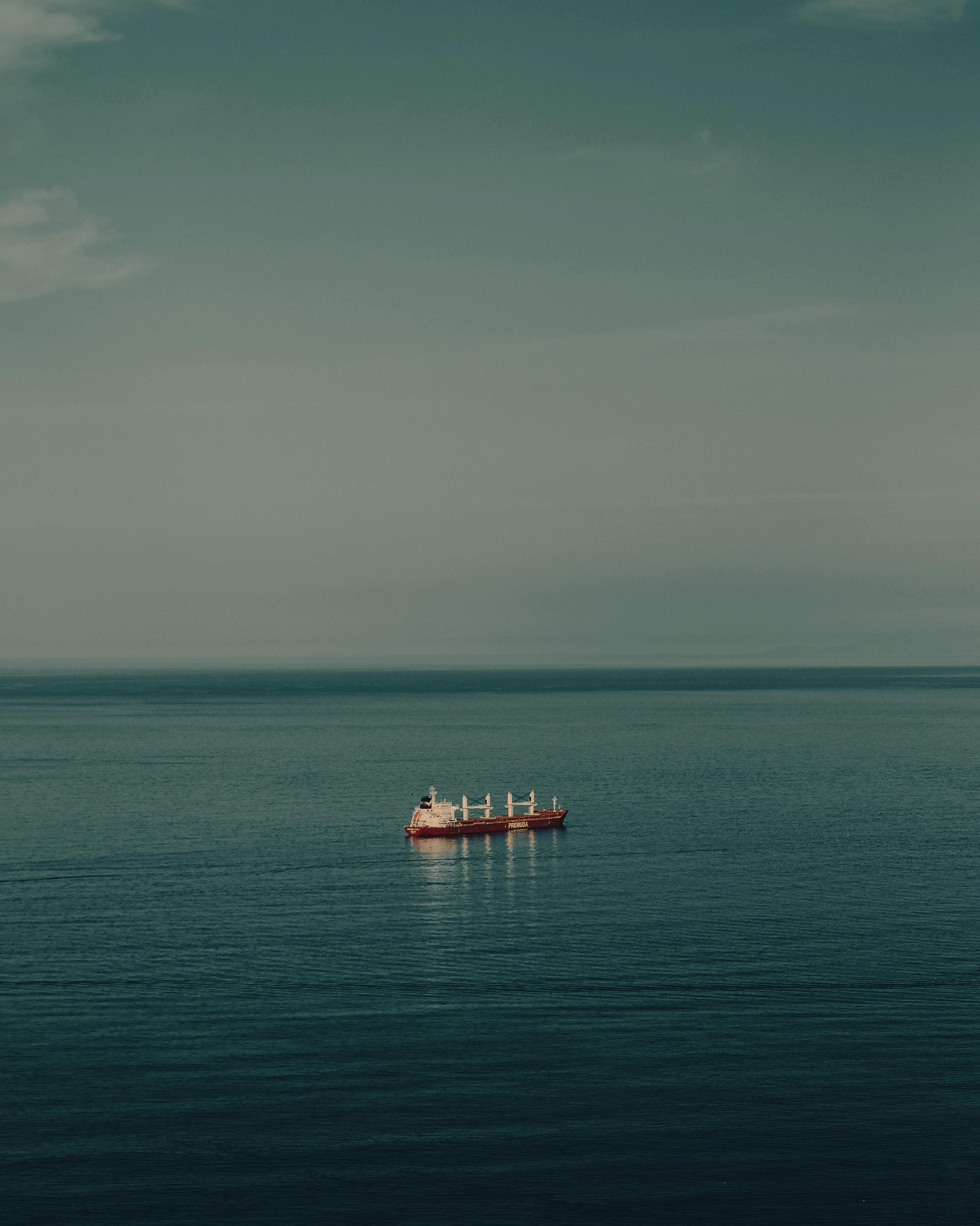 A solitary cargo ship navigates calm blue waters under an expansive sky, capturing serene seascape beauty.