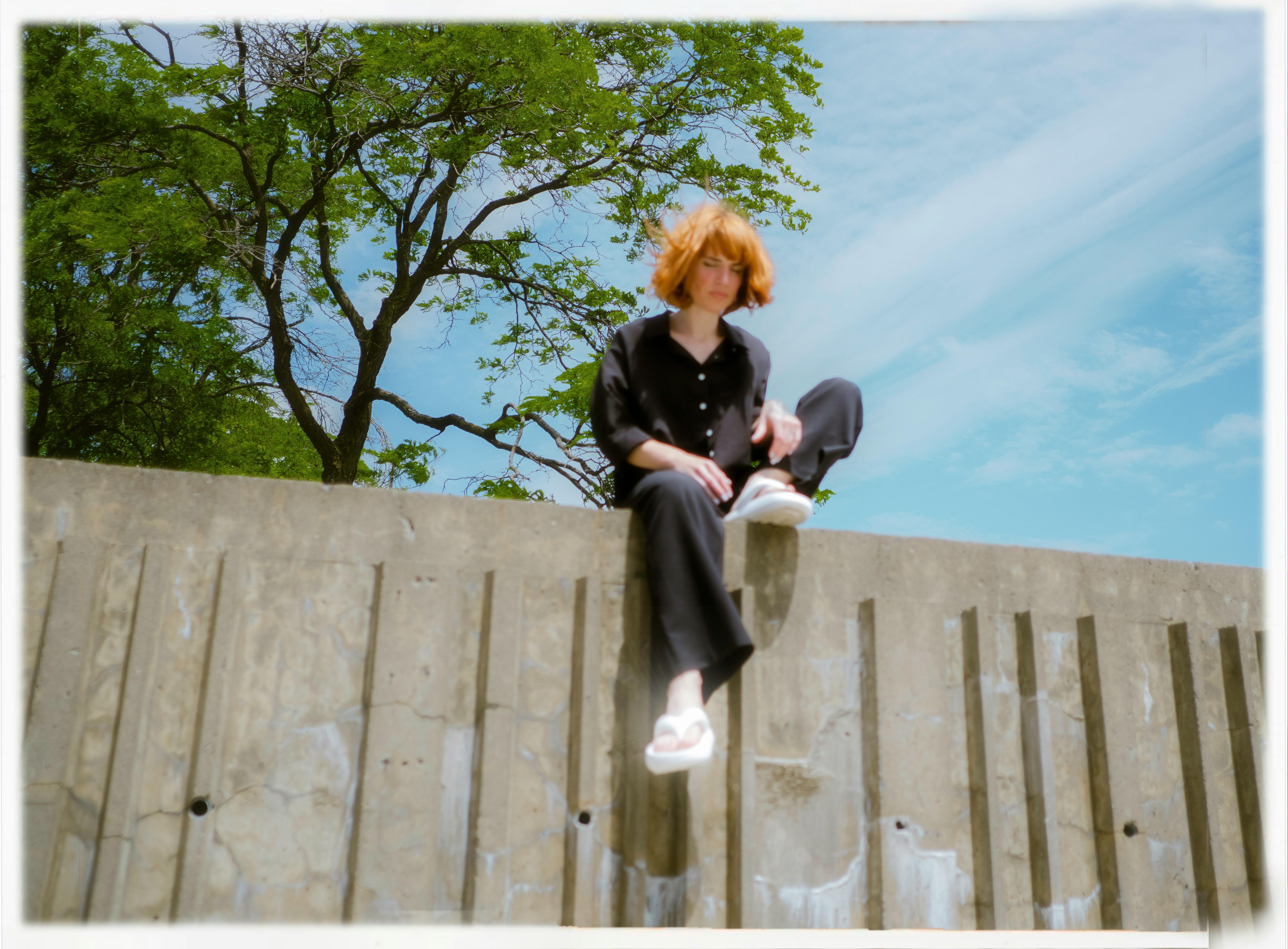 A young woman with red hair sitting on a wall outdoors in Montréal, Canada.