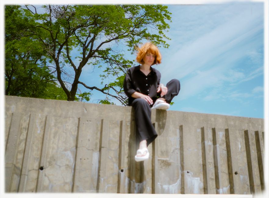 A young woman with red hair sitting on a wall outdoors in Montréal, Canada.
