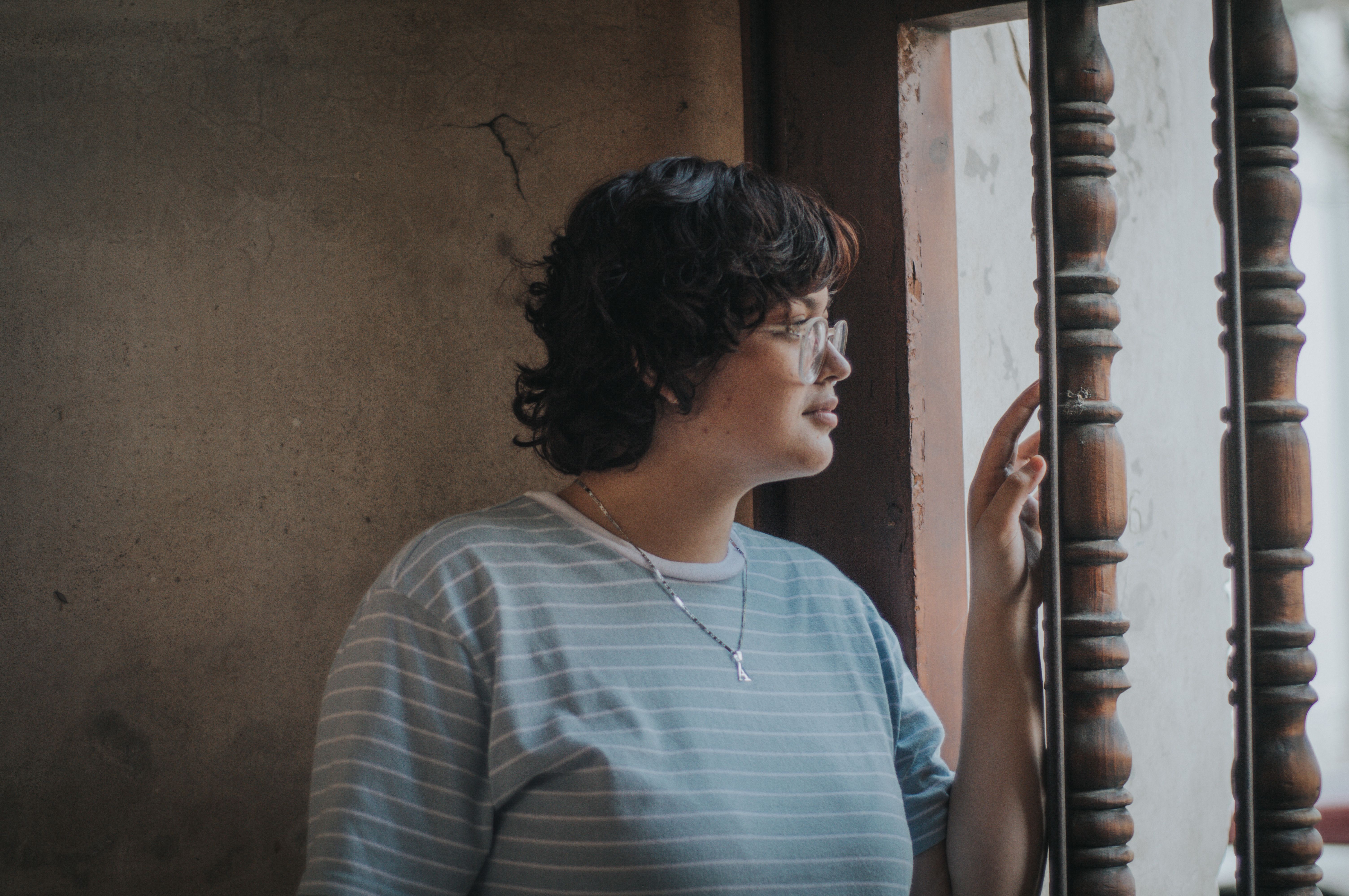 A thoughtful woman with short hair and eyeglasses gazes out a window.