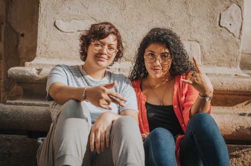 Free Two young women sitting against a stone wall, enjoying a bright sunny day. Stock Photo