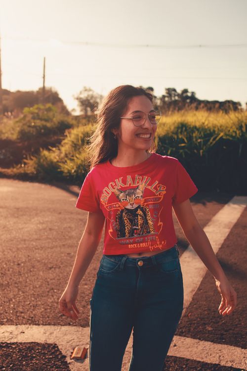 Free Cheerful woman wearing red rockabilly t-shirt smiling on a sunlit street corner. Stock Photo