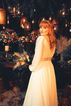 Bride in a vintage wedding dress posing with a rustic bouquet amidst a warm, intimate setting.