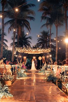 A beautiful outdoor wedding ceremony with decorated aisle and elegant lighting under palm trees.