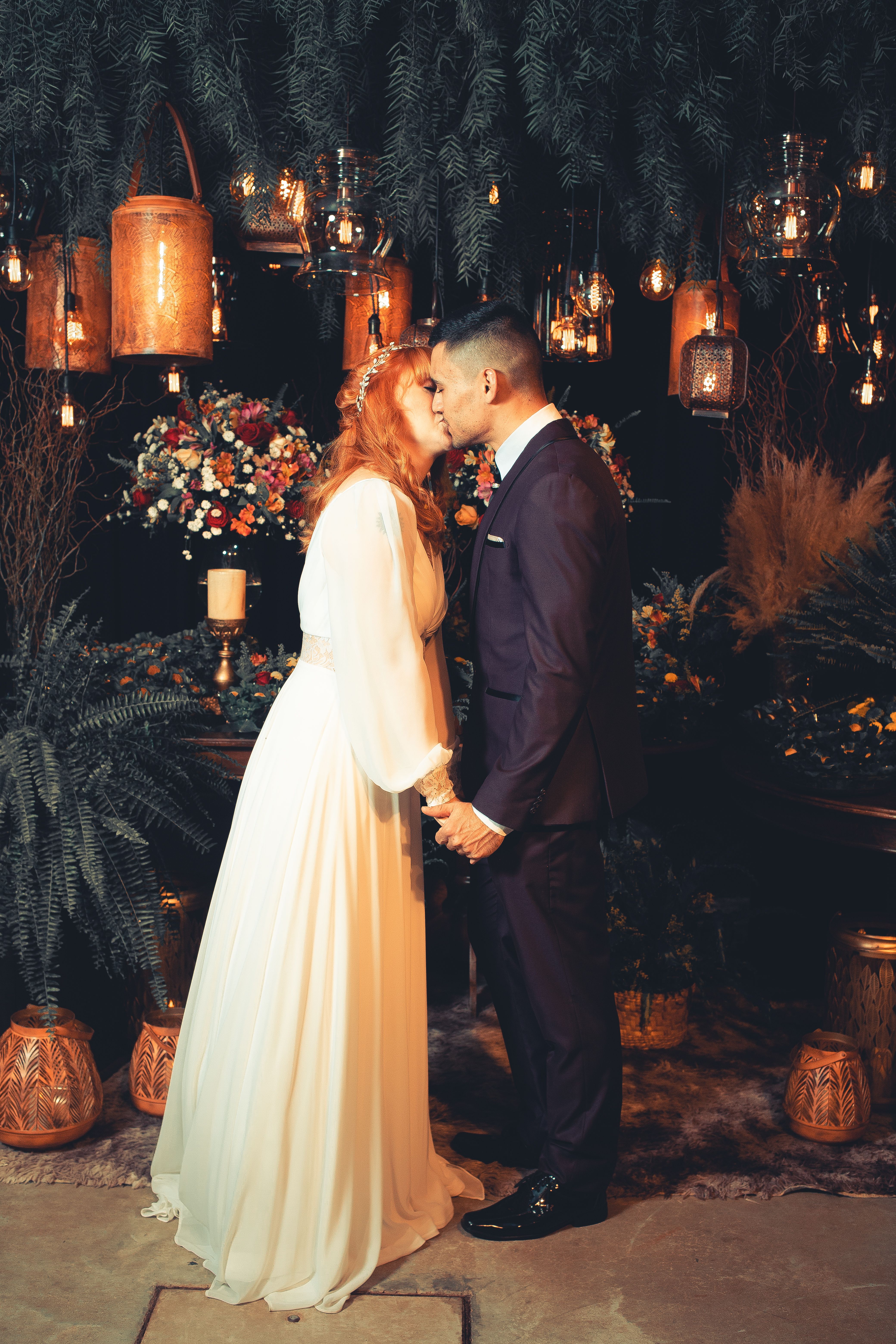 A bride and groom sharing a romantic kiss amidst elegant floral arrangements and warm lighting.