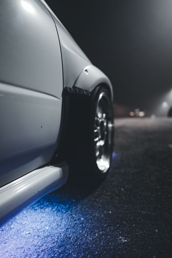 Dark custom wheel under a widened fender, lit by blue underglow