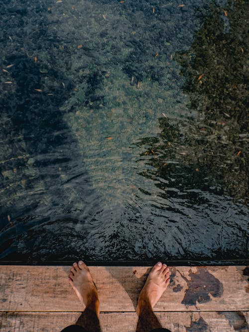 clear pool with feet visible on wooden planks