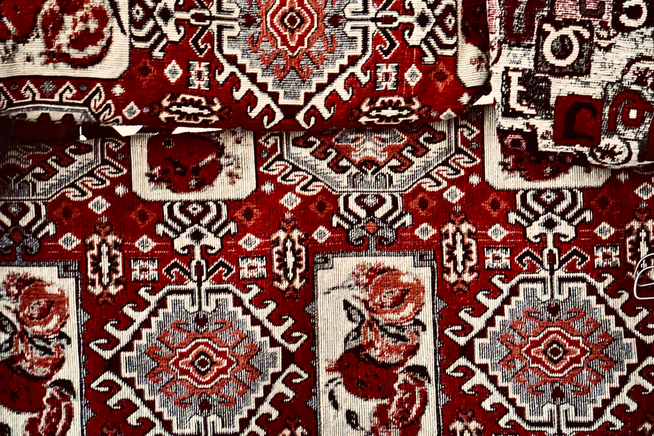 Close-up of a handmade carpet showcasing detailed red and white traditional patterns, emphasizing handcraft.