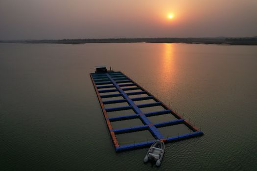 Aerial view of a tranquil fish farm on a calm sea at sunset with a small boat, radiating peace.