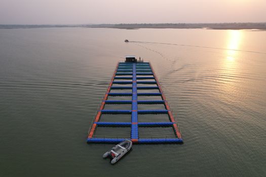 Aerial view of a floating jetty on a calm sea at sunset with moored motorboat.