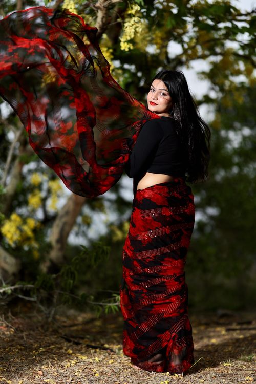 Free A fashionable woman poses gracefully with flowing red and black scarf in nature. Stock Photo
