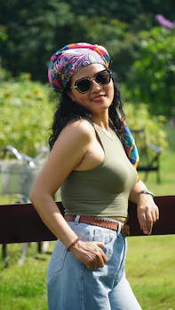 Fashionable woman with colorful headscarf and sunglasses smiling in a sunny park.