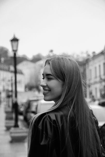 Black and white photo of a smiling woman with long hair walking in a town street.