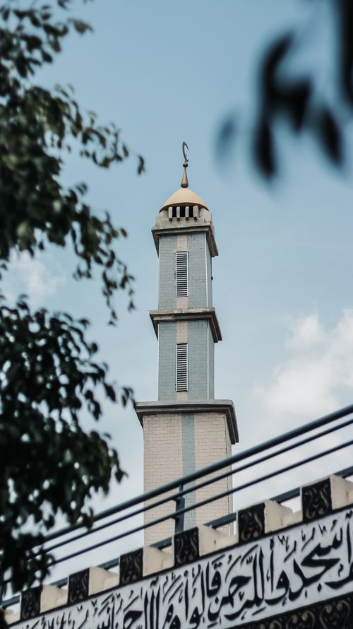 Free Low angle view of a mosque minaret with Arabic calligraphy in foreground and trees framing the composition. Stock Photo